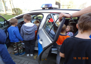 Dzieci z bliska ogladają radiowóz policyjny. Niektóre dzieci są w środku auta.